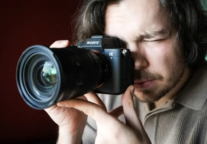 Mężczyzna zamyka oko, patrząc przez wizjer aparatu Sony Alpha 7. Premiera Sony a7 IV budzi emocje.