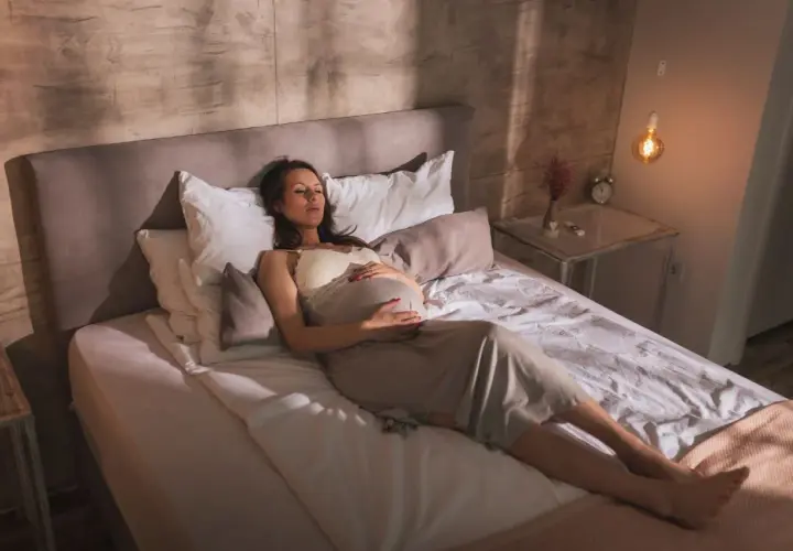 Femme enceinte se repose sur le dos, ventre arrondi, dans une position confortable pour dormir enceinte 1er trimestre.