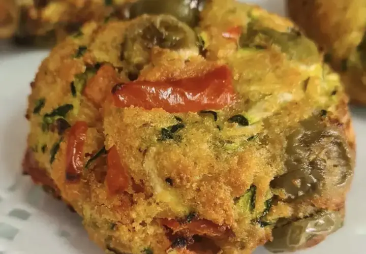 Polpette di zucchine dorate e saporite, con pomodorini e olive verdi, pronte per essere gustate.