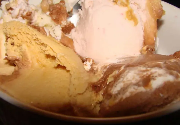 Un tazón lleno de helado de leche cremoso, con sabores de caramelo, fresa y chocolate, adornado con trozos de galleta.