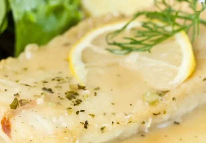 Filete de pescado bañado en una deliciosa salsa de limón para pescado, adornado con una rodaja de limón y eneldo.