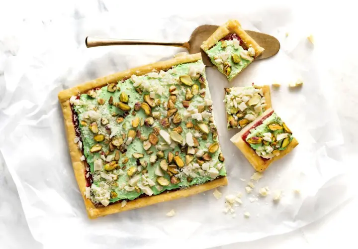 Ciasto z zieloną masą pistacjową i posiekanymi pistacjami, pokrojone na kwadraty.