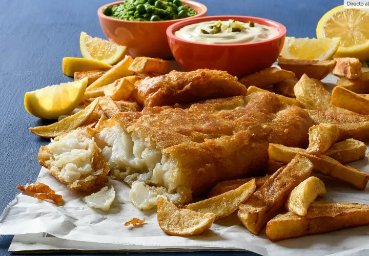 Un delicioso plato de fish and chips, con pescado rebozado crujiente, patatas fritas doradas, guisantes y salsa tártara.