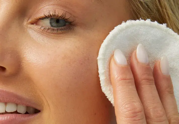 Delikatny peeling na prosaki, który odświeża skórę. Kobieta z blond włosami i niebieskimi oczami stosuje go na twarz.