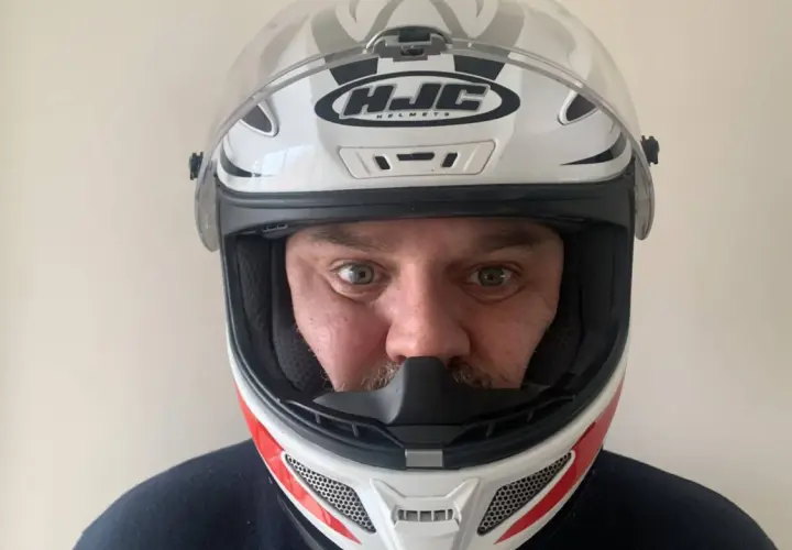 Hombre con casco de moto HJC blanco y rojo, listo para elegir su próxima aventura.