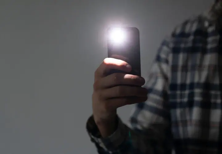 Dłoń trzyma telefon, którego latarka w telefonie rozświetla ciemność.