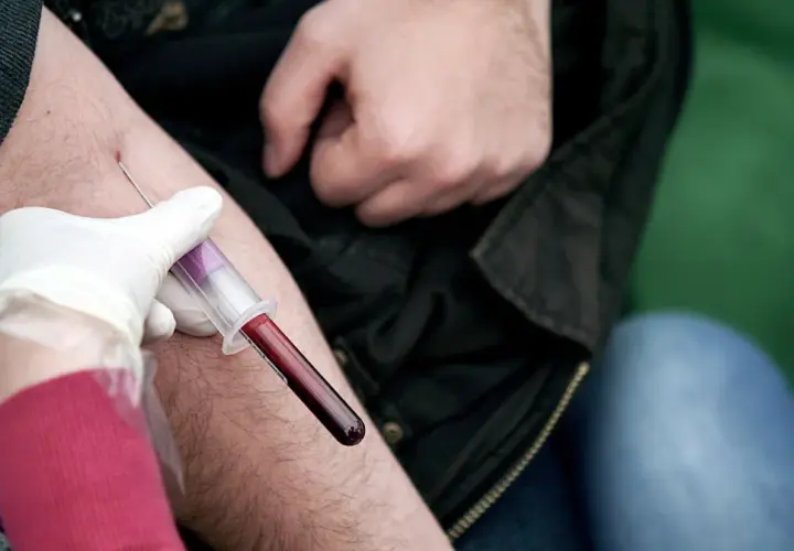Pobieranie krwi do badania. Lekarz w białej rękawiczce pobiera krew do probówki, sugerując, że **ALT AST podwyższone** może być przyczyną.