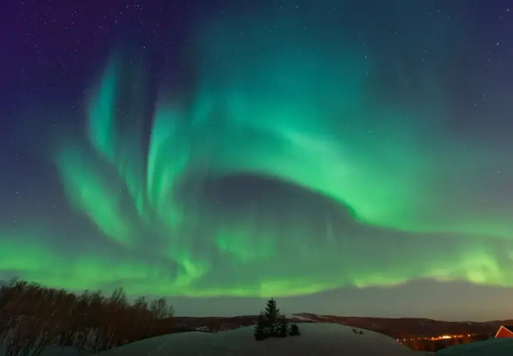Zielona zorza polarna nad śnieżnym krajobrazem w Norwegii. Niebo rozświetlone tańczącymi światłami.