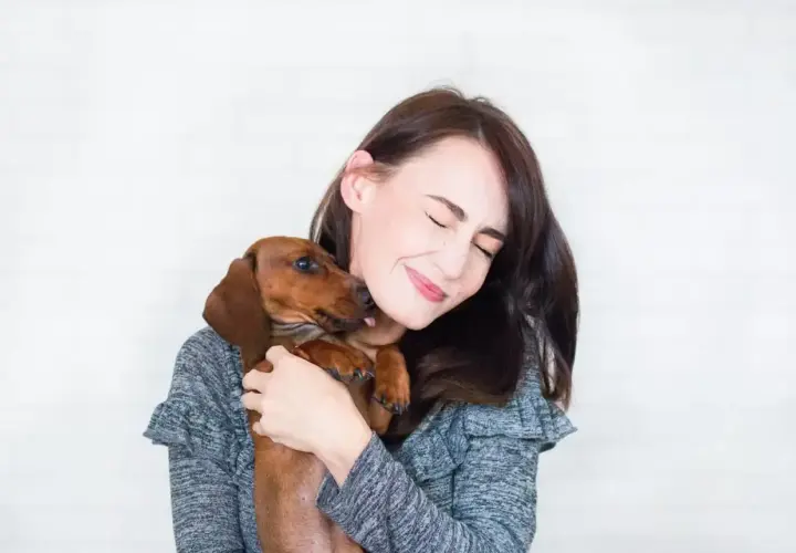 Un perro salchicha le lame la cara a su dueña, que sonríe con los ojos cerrados. Es la prueba de que mi perro me sigue a todas partes.