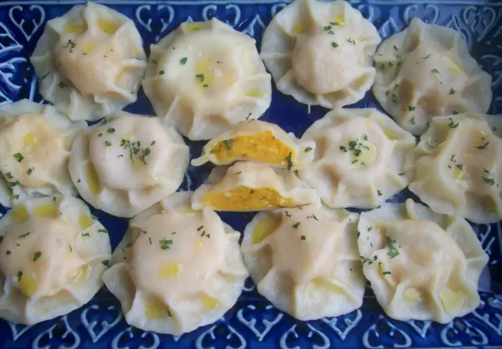 Pyszne pierogi z dynią, polane masłem i posypane natką pietruszki, ułożone na niebieskiej tacy.