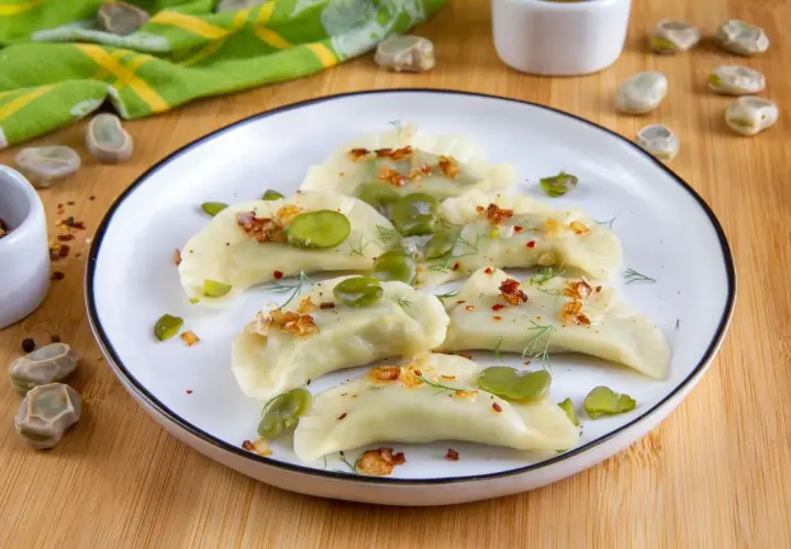 Pyszne pierogi z bobem, posypane skwarkami i koperkiem, prezentują się apetycznie na talerzu.
