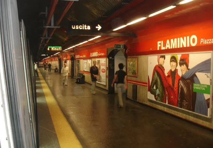 Stazione della metro Roma Nord, banchina con persone in attesa, cartelloni pubblicitari e indicazioni per l'uscita.