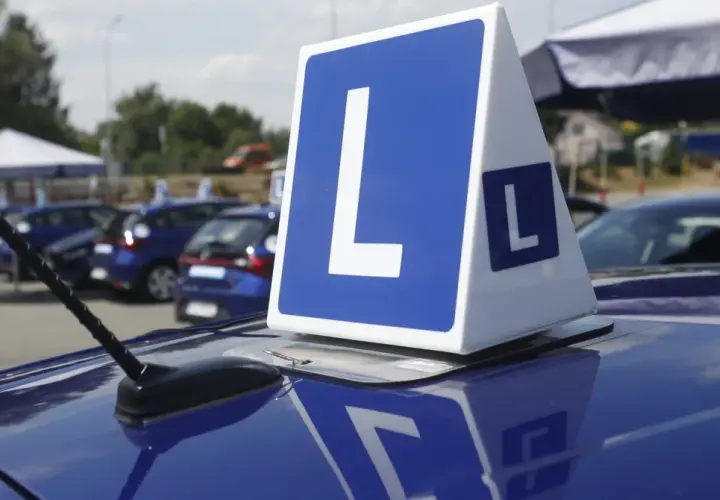 Niebieskie samochody z literą "L" na dachu, symbolizujące naukę jazdy i zasady egzaminu na prawo jazdy.