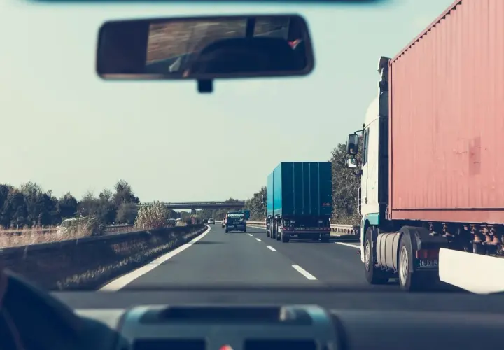 Widok z kabiny samochodu na autostradzie z ciężarówkami i innymi pojazdami.