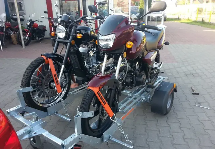 Dwa motocykle na przyczepie, zabezpieczone pasami.