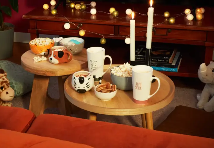 Tavolini bassi con tazze a tema animale, popcorn e biscotti, perfetti per una serata cinema a casa.