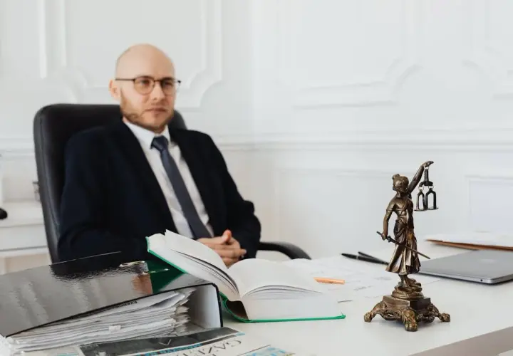 Prawnik w garniturze analizuje dokumenty dotyczące kosztów notarialnych przy zakupie mieszkania. Na biurku Statua Temidy i otwarte księgi.