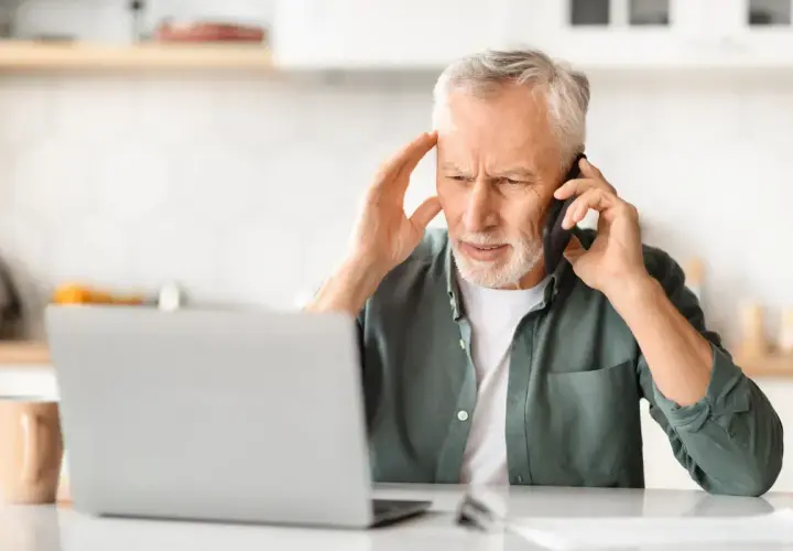 Zmartwiony mężczyzna rozmawia przez telefon, trzymając się za głowę. Może szuka siła wyższa powody problemów z laptopem.