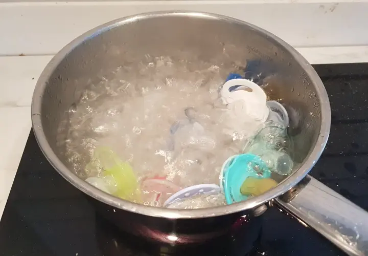 Flera färgglada nappar ligger i en kastrull med kokande vatten. Det är dags att koka nappar för hygien.