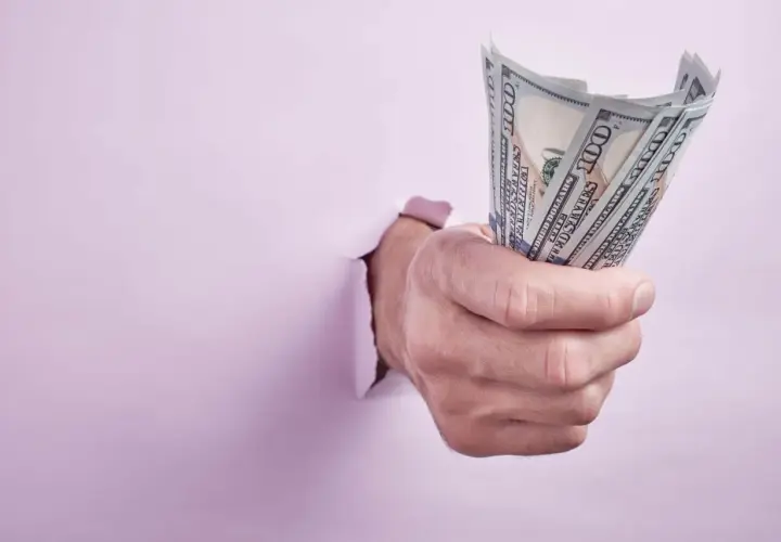 Dłoń przebija się przez różową ścianę, trzymając plik banknotów 100 dolarowych. Może to symbolizować zwrot kaucji od byłego lokatora.