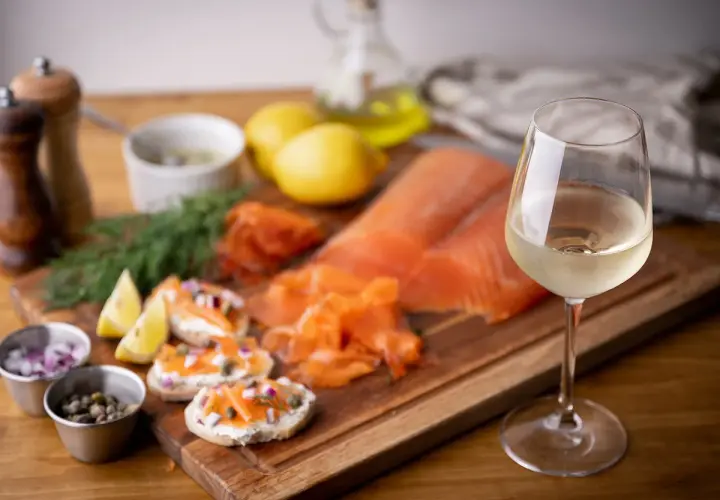 Un verre de vin blanc frais accompagne un saumon fumé et des toasts. Parfait pour savoir quel vin avec du saumon en papillote.