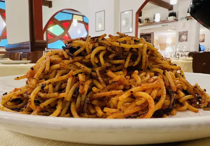 Un piatto di spaghetti con pomodoro e basilico, un classico su cosa mangiare a Bari. Il tutto servito in un ristorante con vetrate colorate.