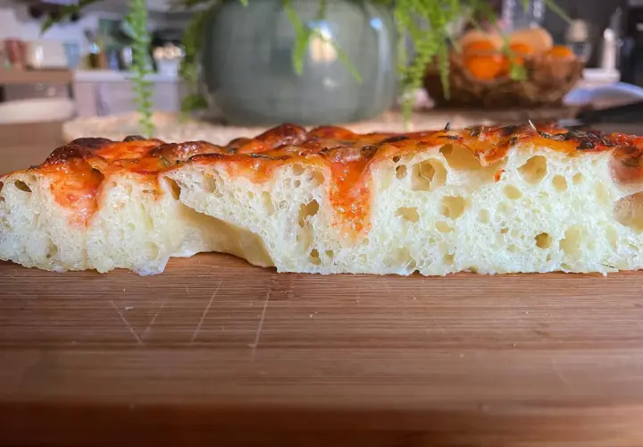Fetta di focaccia soffice e alveolata, con pomodoro e formaggio filante. Perfetta per uno spuntino o un pasto veloce.