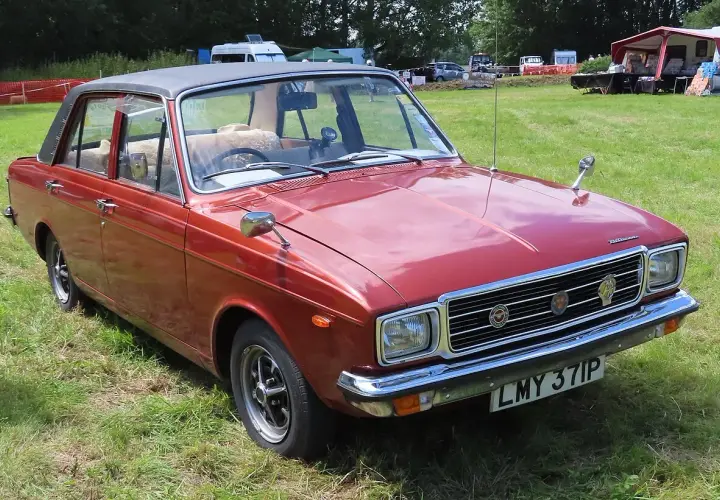 Röd Hillman bil med svart vinyltak, parkerad på en gräsmatta vid ett evenemang.
