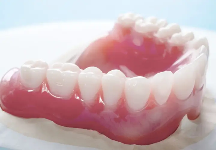 Un primo piano di una dentiera rosa con denti bianchi. La dentiera mi fa vomitare.