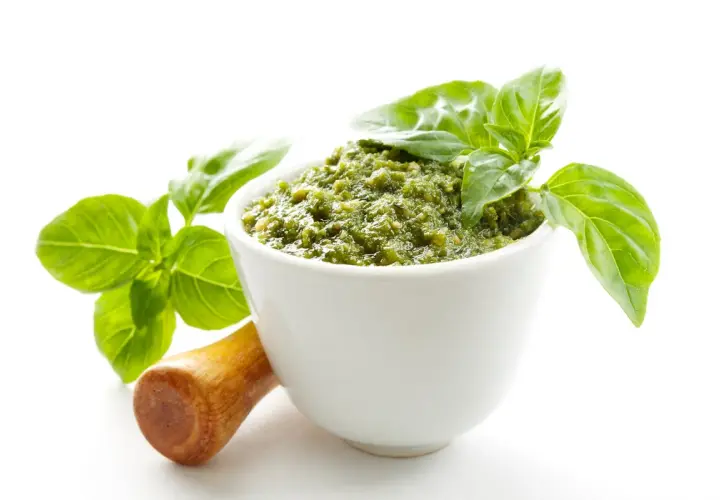 Aksamitne, zielone pesto w białej miseczce, ozdobione listkami bazylii. Obok drewniany tłuczek. To najlepsze pesto, jakie możesz sobie wyobrazić!