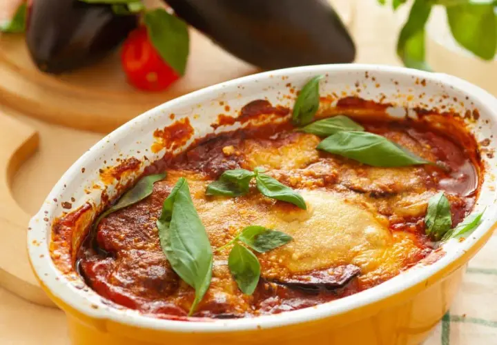 Aubergine parmigiana dorée et gratinée, garnie de feuilles de basilic frais. Un plat réconfortant prêt à être dégusté.
