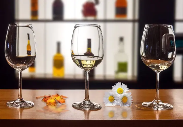Trzy kieliszki na drewnianym blacie. Jak usunąć zapach alkoholu z kieliszka przed ponowną degustacją? Jesienne liście i kwiaty dodają uroku.