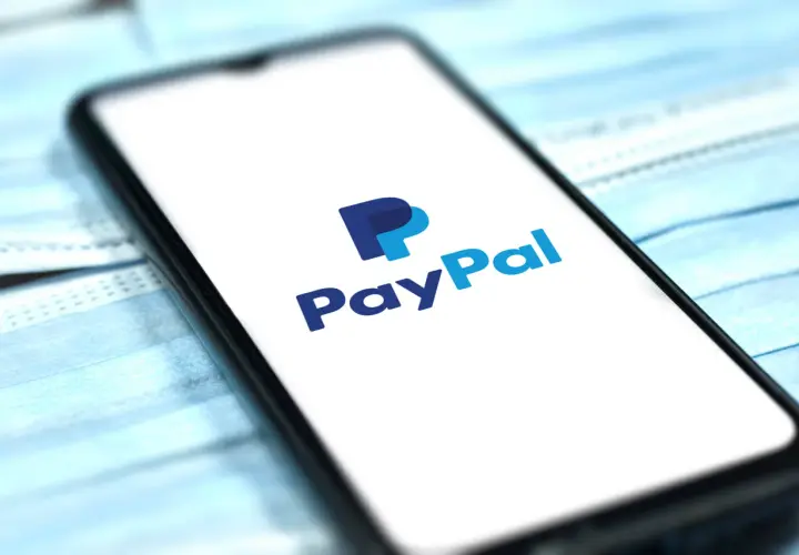 Smartfon z logo PayPal na ekranie, leżący na niebieskich maseczkach ochronnych. Szybkie i bezpieczne płatności online.