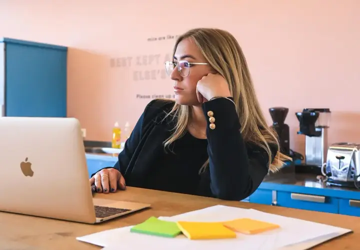 Kobieta w okularach zastanawia się, ile trwa staż z urzędu pracy, patrząc na laptopa. Na biurku kolorowe karteczki.