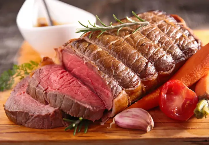 Un rôti de bœuf de 1k500, saignant et savoureux, servi avec des carottes, une tomate et de l'ail. Le temps de cuisson parfait pour ce délice.