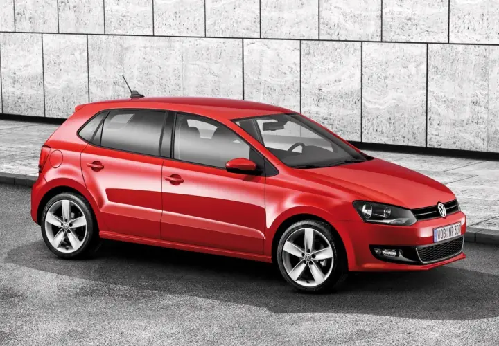 Czerwony Volkswagen Polo 6R z felgami aluminiowymi stoi na tle nowoczesnej, betonowej ściany.