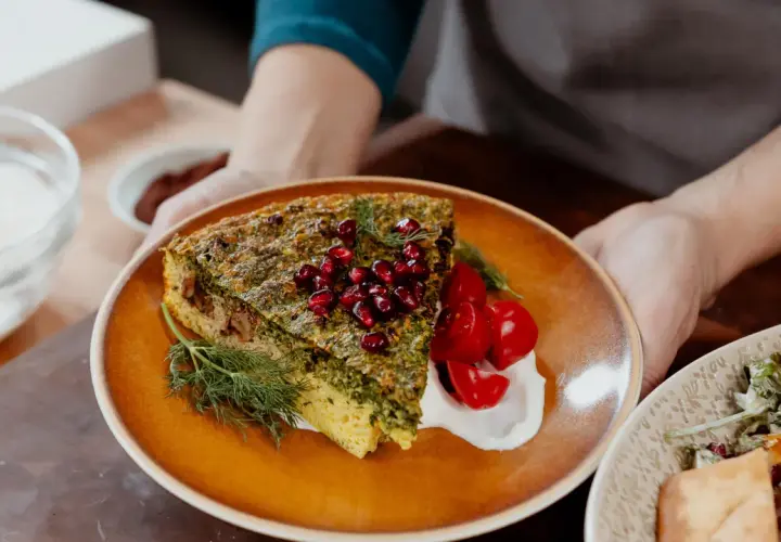 Une part de kuku sabzi, une tarte aux herbes persane, garnie de grenades et de tomates cerises, servie avec une touche de yaourt.