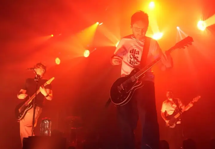 Koncert Myslovitz. Wokalista i gitarzysta na scenie, w tle basista. Czerwone światła podkreślają energię utworów.