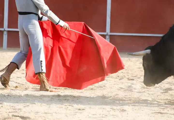 Torero con capote rojo se enfrenta a un toro bravo, evocando la tradición de los encierros más antiguos de España.