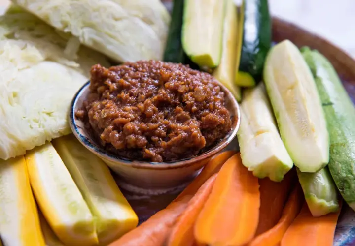 A bowl of savory miso dip is surrounded by fresh, colorful crudités: sliced zucchini, yellow squash, carrots, and cabbage wedges, ready for dipping.