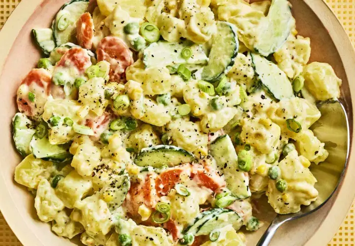 A creamy Japanese potato salad with chunks of potato, cucumber, peas, and carrots, garnished with green onions and black pepper.