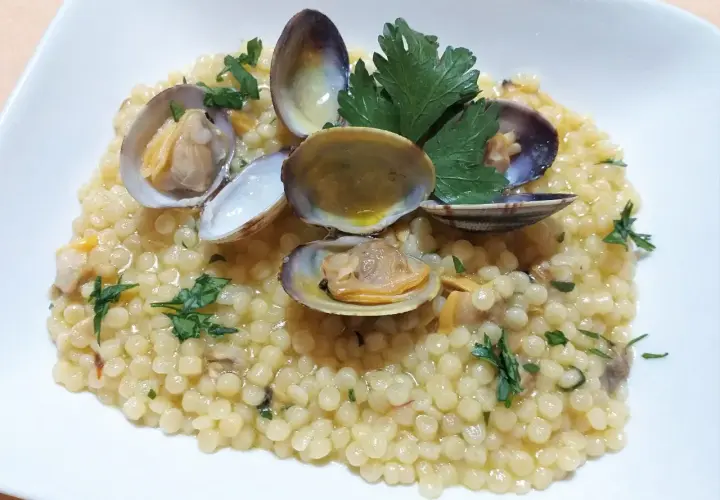 Piatto di fregola con vongole, profumata al prezzemolo e condita con un filo d'olio. Un classico della cucina sarda.