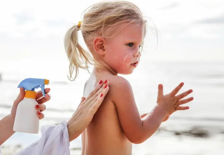 Ochrona przed słońcem jest kluczowa, by uniknąć oparzeń słonecznych u dzieci. Mama smaruje córkę kremem na plaży.