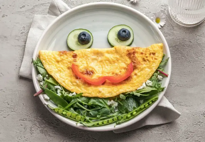 Uśmiechnięta omletowa buzia z oczami z ogórka i borówki, ułożona na sałatce z groszkiem. Idealny comfort food na dobry początek dnia.