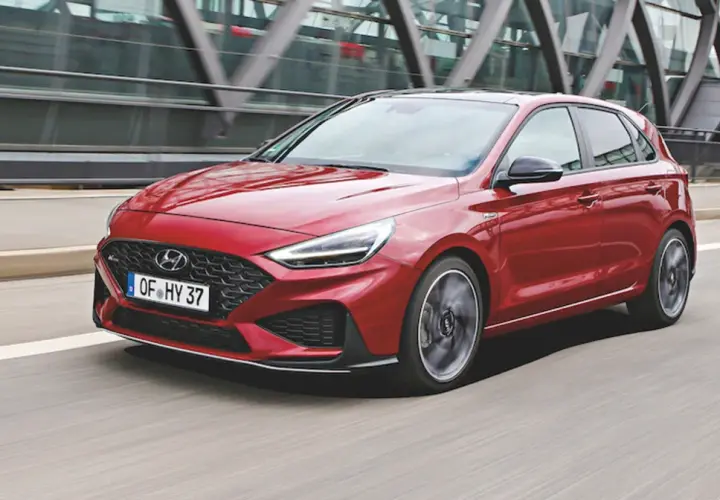 Czerwony Hyundai i30 2024 w wersji N Line pędzi po drodze, z nowoczesną atrapą chłodnicy i ostrymi światłami LED.