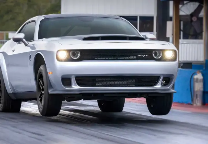 Srebrny Dodge Challenger SRT na torze wyścigowym, z przednimi kołami lekko uniesionymi nad asfaltem.