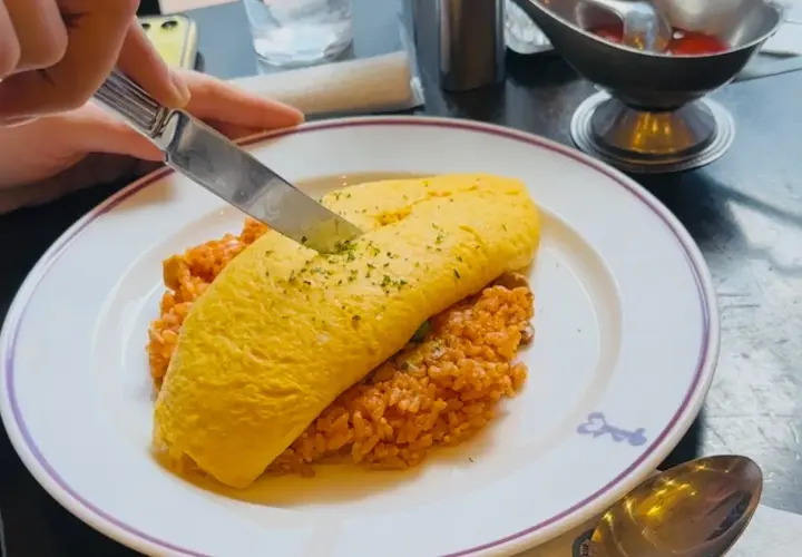 A knife cuts into a fluffy omelet atop rice, a delicious example of Japanese dishes with cheese.