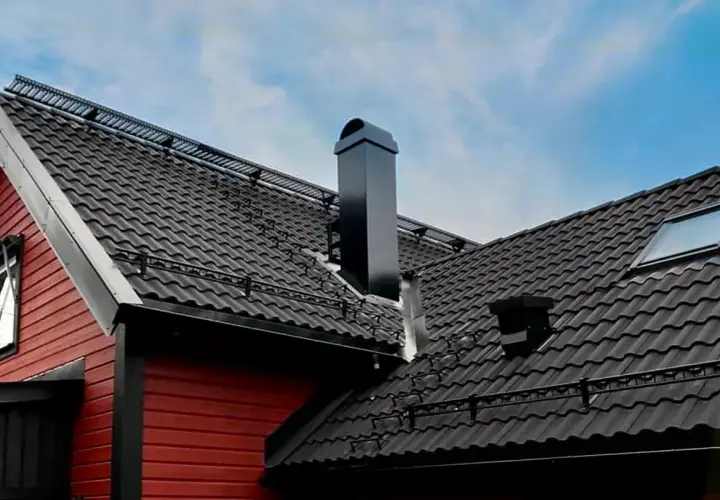 Svart, modern skorsten på ett tak med mörka takpannor. En röd träfasad syns till vänster.