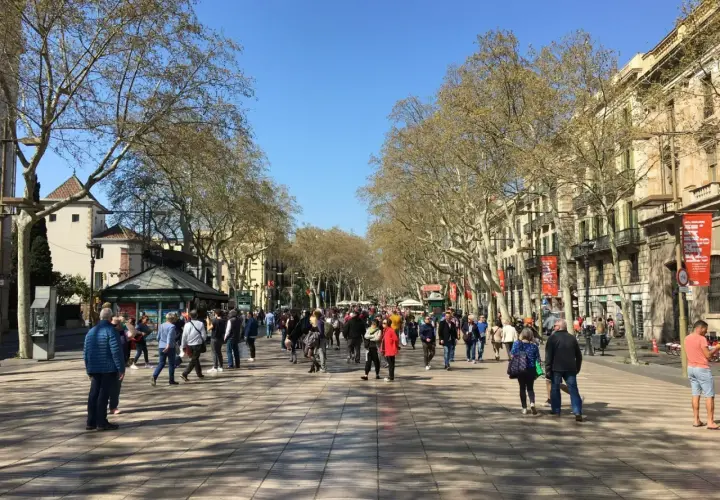 Tłum ludzi spaceruje po szerokim deptaku Las Ramblas w Barcelonie, otoczonym drzewami i budynkami.