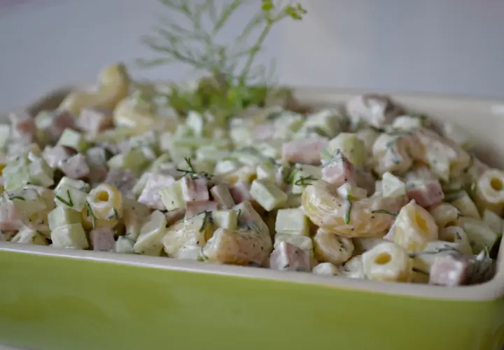 Pyszna sałatka z makaronem, szynką, ogórkiem i serem, udekorowana świeżym koperkiem.